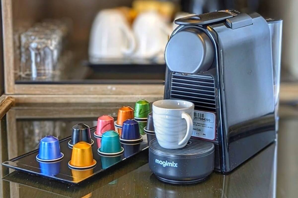 A coffee machine with a tray of colorful cups and a single white cup in front of it.