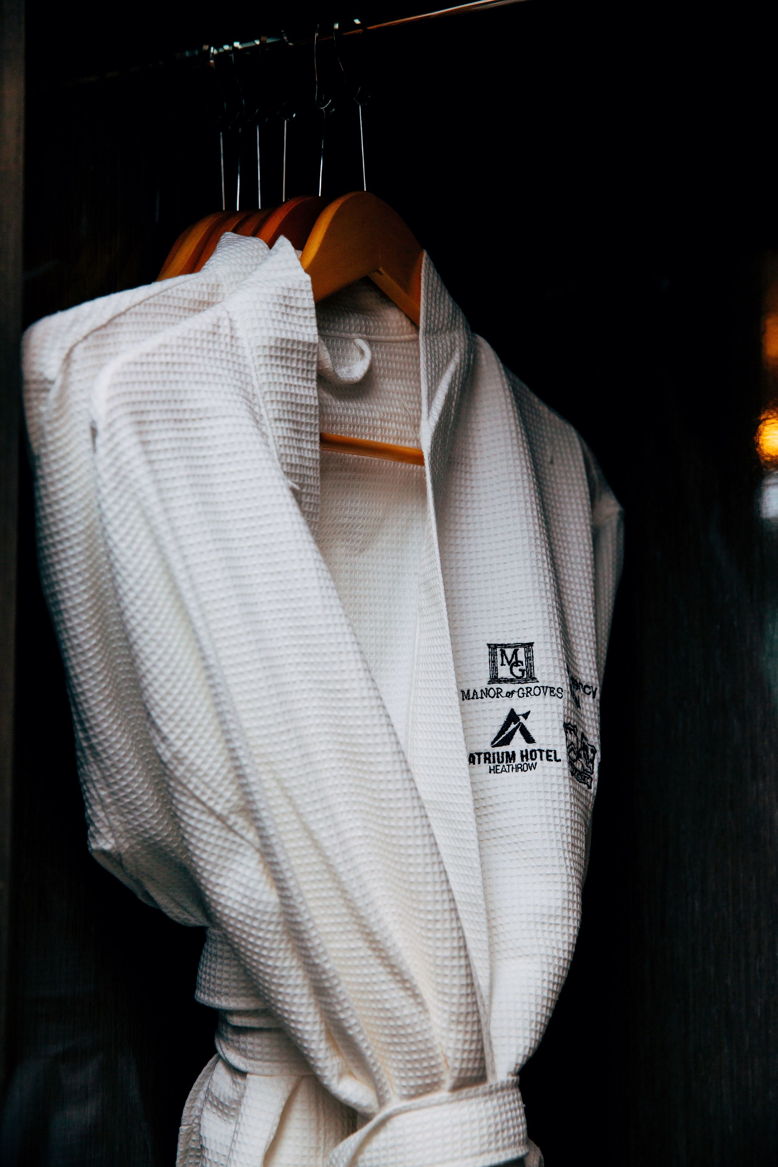 Une blouse blanche est suspendue à un cintre en bois, ornée d’un logo et d’une inscription indiquant qu’elle provient de l’hôtel Atrium, à Heathrow.