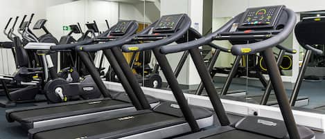 Une rangée de tapis de course dans une salle de sport, avec un téléviseur fixé au mur.
