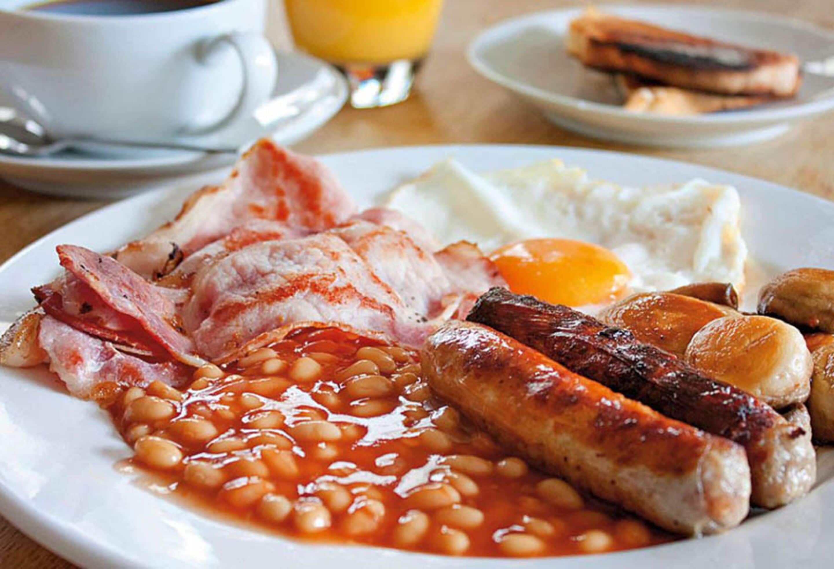 Un plato de desayuno con tocino, salchichas, huevos y frijoles.
