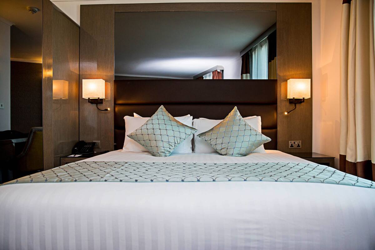 A hotel room with a large bed, two wall-mounted lamps, and a telephone on the nightstand.