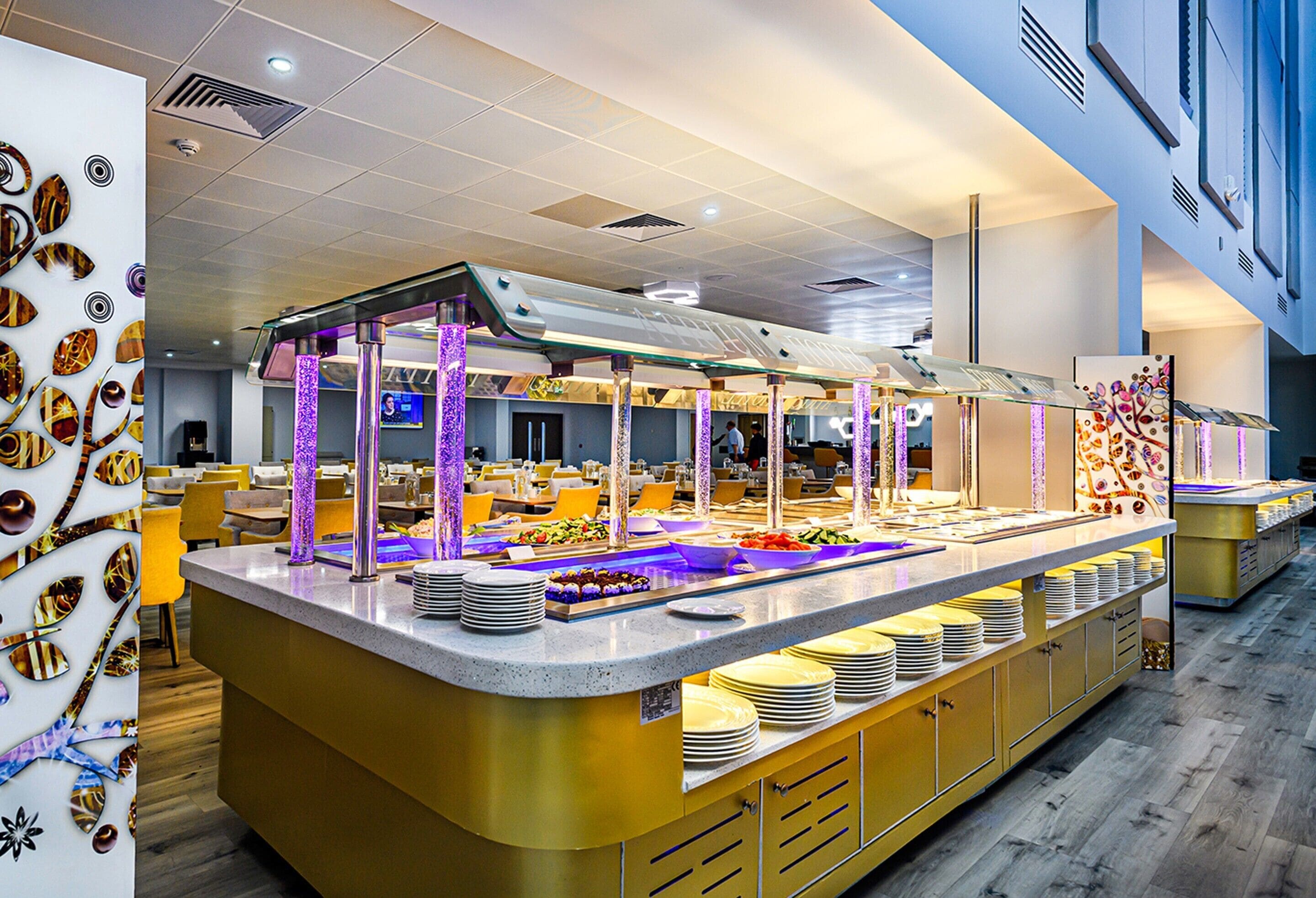A buffet setup with multiple serving stations, a central serving area, and a decorative wall with leaf patterns.