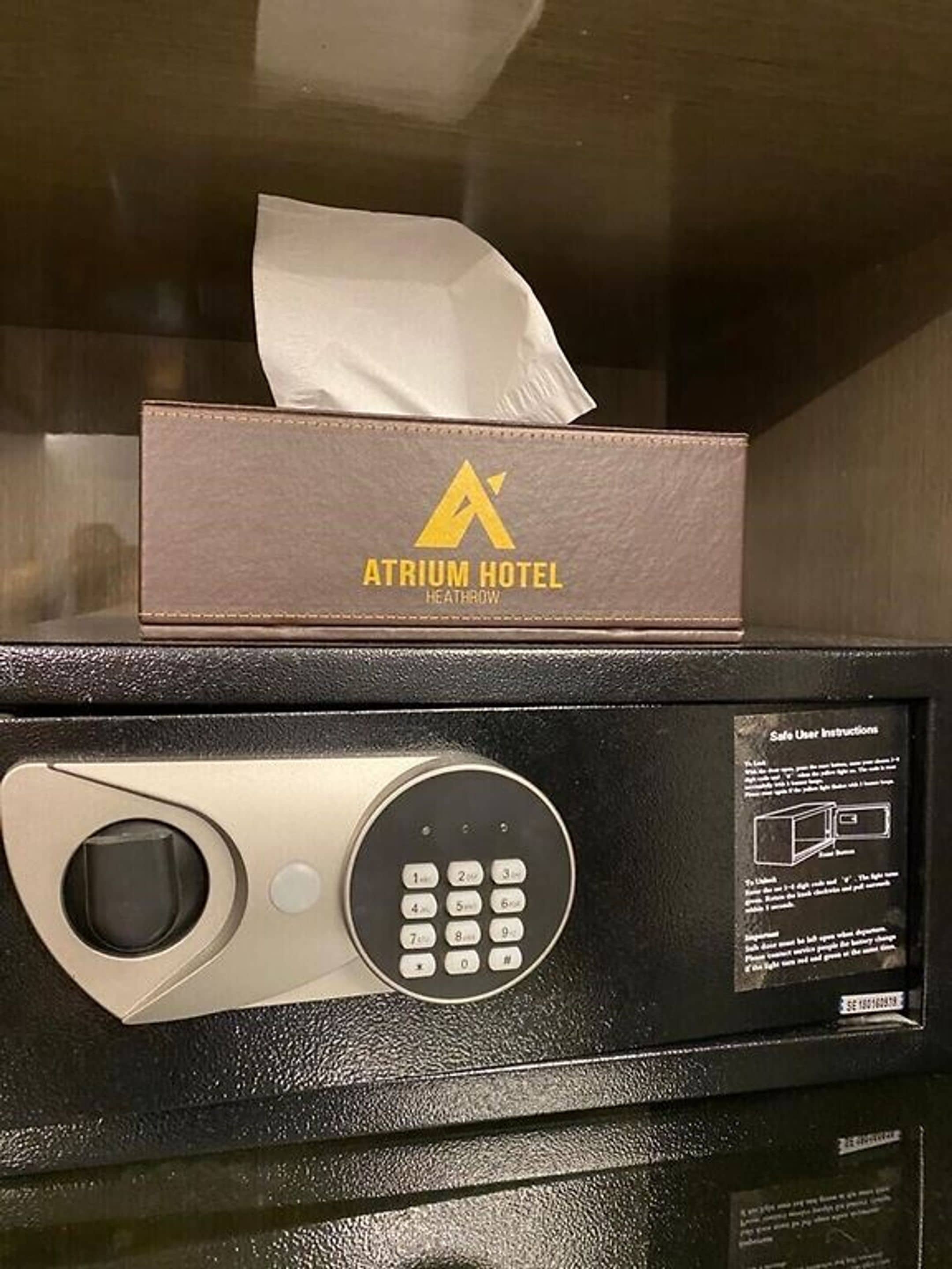 A minibar with a tissue box labeled "Atrium Hotel Heathrow" and a keypad.
