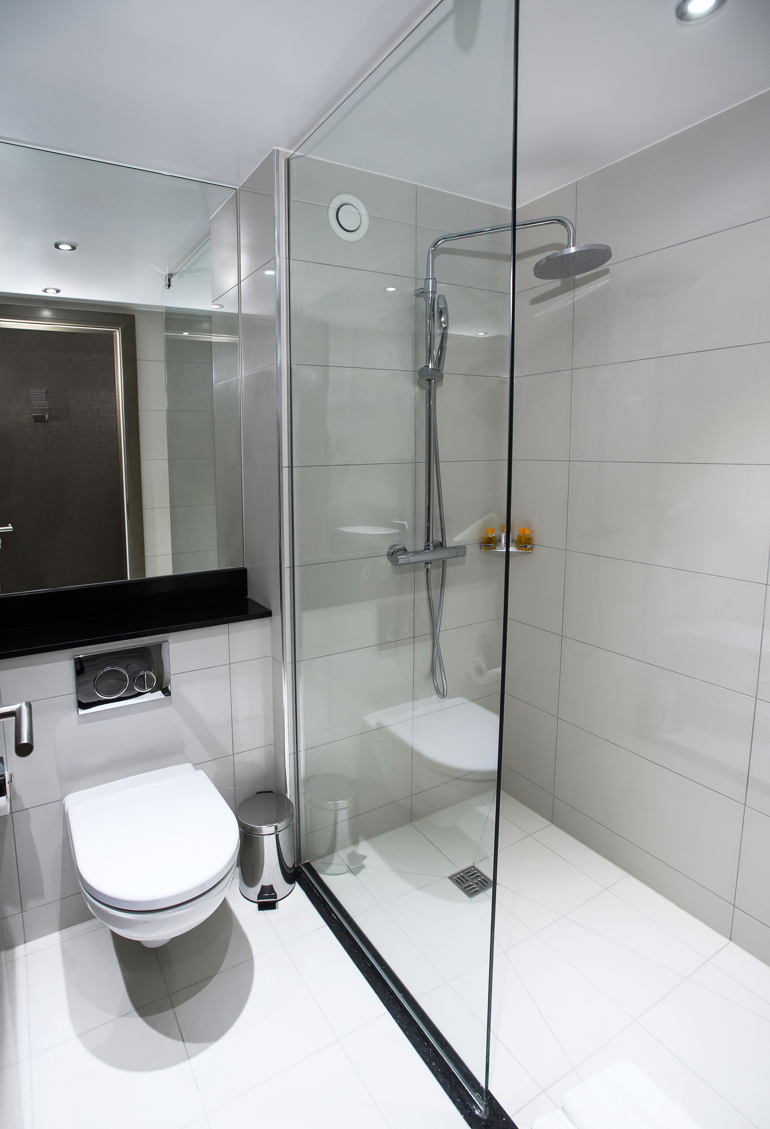 Une salle de bain moderne avec une douche à parois de verre, des toilettes blanches et un plan de toilette noir.