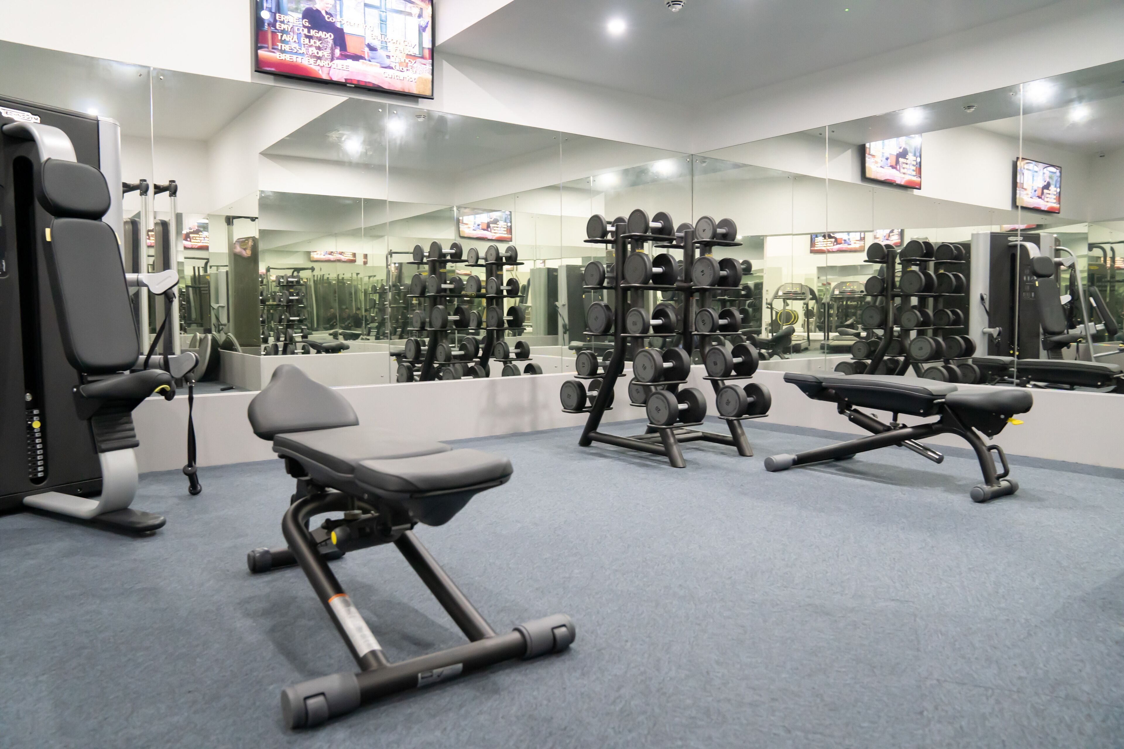 Ein Fitnessstudio mit Trainingsgeräten, Spiegeln und Fernsehbildschirmen.