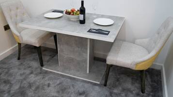 A dining table with two chairs, a bowl of fruit, a bottle of wine, and two glasses.