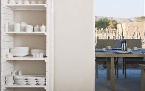 Un comedor con una mesa lista para dos, un mueble blanco con vajilla, y vistas a un paisaje montañoso.