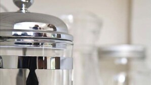 A stainless steel water dispenser with a clear glass container and a metal spout.