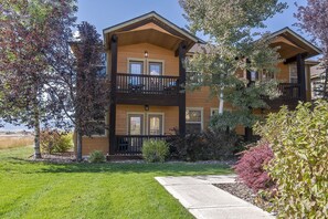 A two-story building with a balcony on the second floor, a front porch, and a well-maintained lawn. - Book Affordable Luxury Condo For All Seasons, Discounted Monthly Winter Rates. (Driggs)