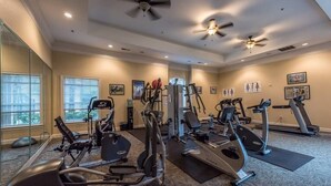 Un gimnasio con diverso equipo de ejercicio, amplias ventanas y ventiladores de techo.