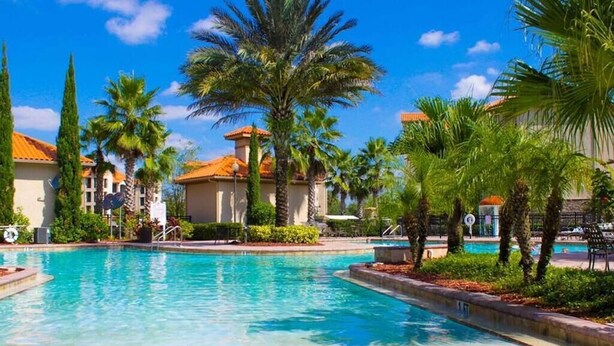 Un área de piscina con palmeras y edificios al fondo.