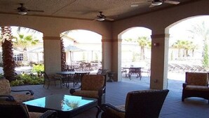 Un patio exterior con mobiliario de mimbre, una mesa con superficie de vidrio y un ventilador de techo.