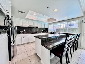 A modern kitchen with white cabinets, a granite countertop, and a large island with bar stools.