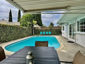 A covered outdoor area with a swimming pool, a table with chairs, and a lamp.