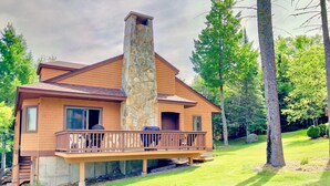 A two-story house with a stone chimney, a balcony with outdoor furniture, and a well-maintained lawn.