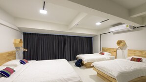 Une chambre d’hôtel avec trois lits simples, une grande fenêtre avec des rideaux foncés et une tête de lit en bois.