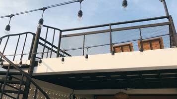 A rooftop terrace with a metal railing, a fan, and string lights.