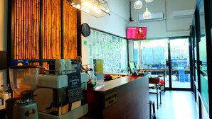 L'intérieur d'un café, avec un mur en bois, un tableau affichant le menu, une horloge et une vue sur la rue.