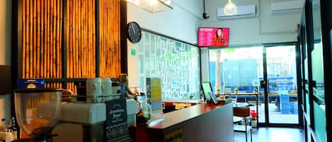 A coffee shop interior with a wooden wall, a menu board, a clock, and a view of the street outside.