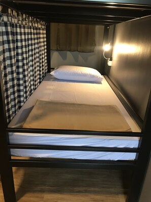 A bunk bed with a headboard, a pillow, and a bedside lamp. - Arun Old Town Hostel (Bangkok)