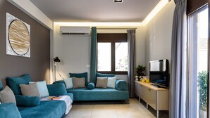 A modern living room with a teal sofa, a flat-screen TV, and a large window with curtains. - City Breeze Apartment (Chania)
