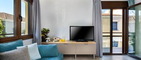 A modern living room with a sofa, a flat-screen TV, and a small table with books and a pitcher of juice.