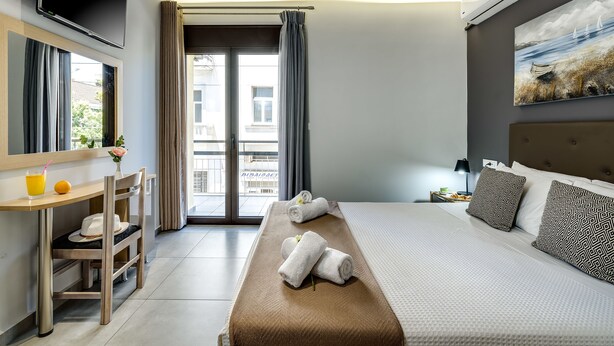 A hotel room with a bed, a desk, a chair, a TV, and a painting on the wall. - City Breeze Apartment (Chania)