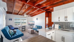 L’intérieur chaleureux d’un chalet avec un plafond en bois, un coin repas, un salon doté d’un canapé et d’une télévision, et une cuisine avec des meubles blancs.