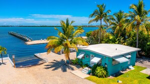 Un bâtiment turquoise doté d’un toit plat, une jetée en béton s’étendant dans l’eau et des palmiers qui entourent la propriété.
