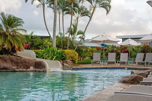 Área de piscina com espreguiçadeiras, guarda-sóis e palmeiras.