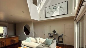 Amplia sala de estar con techo alto, un ventanal grande y una cocina moderna.