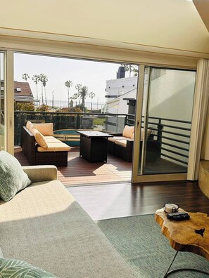 A modern living room with a large sliding glass door leading to a balcony with a pool, furnished with sofas and a coffee table.