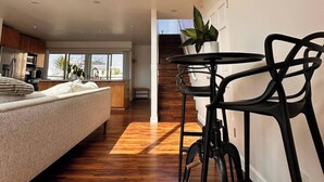 Amplia sala de estar con techo alto, piso de madera, un sofá, una mesa de comedor con sillas y una escalera que sube a un nivel superior.