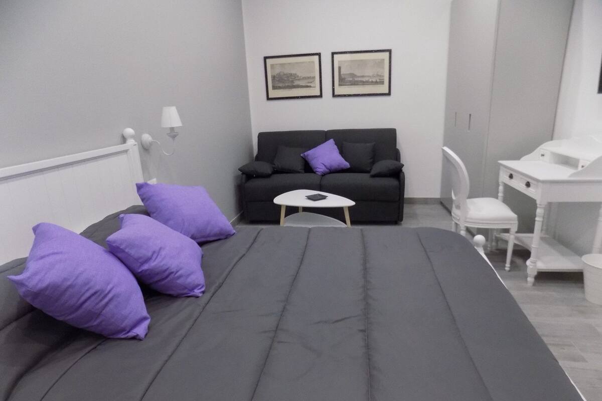 A bedroom with a bed, a small table, a sofa, and a chair.