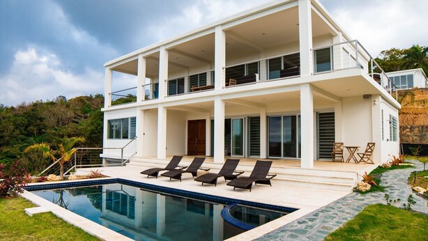 A modern two-story house with a swimming pool, outdoor seating, and a stone pathway.