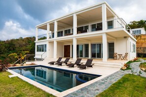A modern two-story house with a swimming pool, outdoor seating, and a stone pathway.