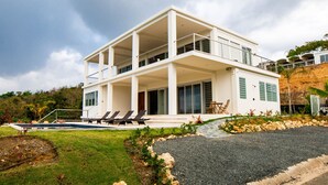 A modern two-story house with a balcony, a swimming pool, and a well-maintained garden.