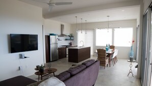 A modern living room with a large sofa, a flat-screen TV, and a dining area with a table and chairs.