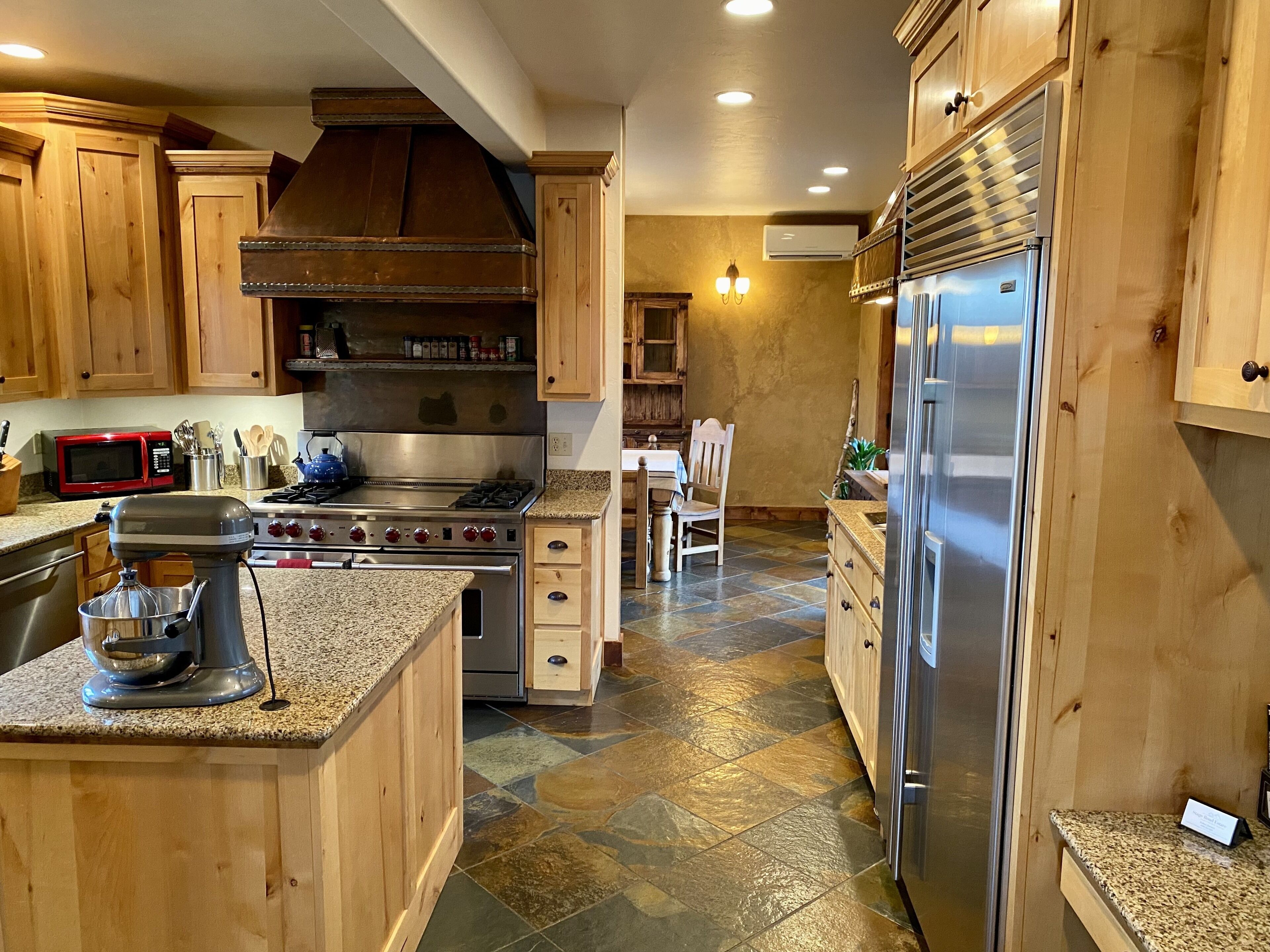 Una cocina con gabinetes de madera, estufa de acero inoxidable, refrigerador y encimera de granito.