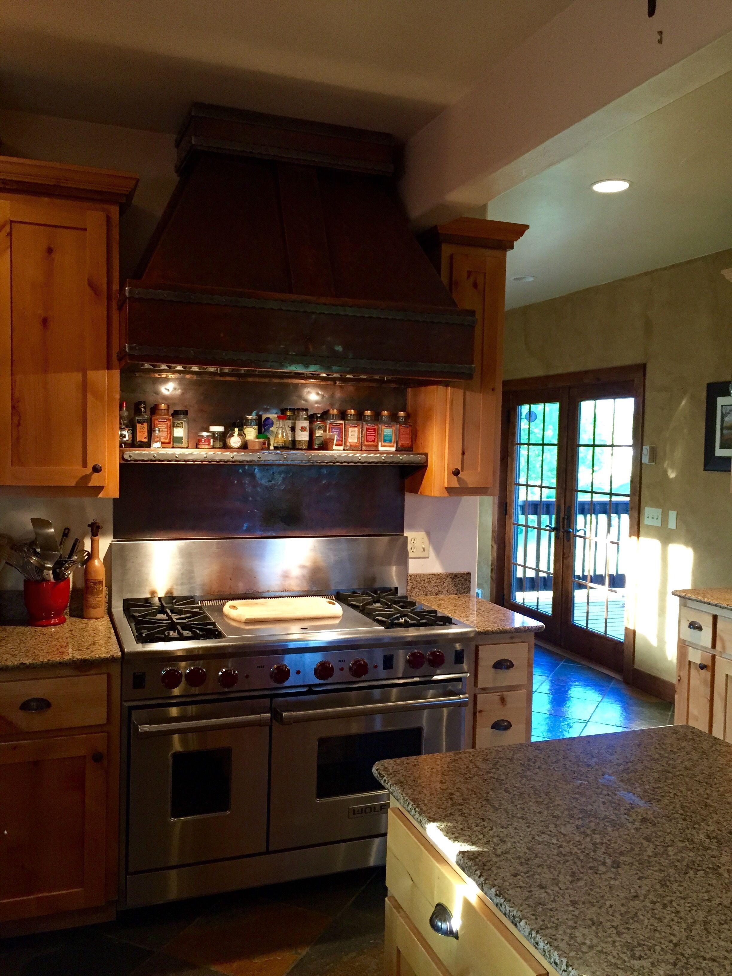 A kitchen with a stainless steel stove, oven, and a wooden cabinet with spice bottles.