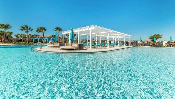 Una piscina azul cristalina con un pabellón blanco y sillones de descanso.