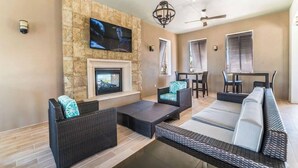 Una sala de estar moderna con muebles de mimbre, una chimenea y un televisor de pantalla plana montado sobre una pared de piedra.