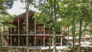A multi-story log cabin with a balcony, surrounded by trees and a stone wall. - 200-Acre Group & Reunion Lodge near Cook Forest — PA WILDS, Sleeps 18 (Shippenville)