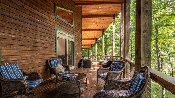 A wooden deck with wicker furniture and a glass door leading to a covered area. - 200-Acre Group & Reunion Lodge near Cook Forest — PA WILDS, Sleeps 18 (Shippenville)