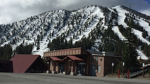 A building with a red roof and a brown facade, situated in front of a snow-covered mountain with dense forests.