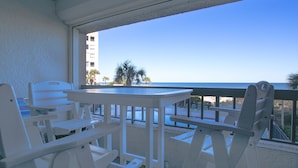 Un balcó amb moble blanc, vista a la platja i un edifici al fons.