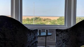 Ett rum med ett stort, utåtbuktande fönster med utsikt över en strand, två stolar och ett litet bord.