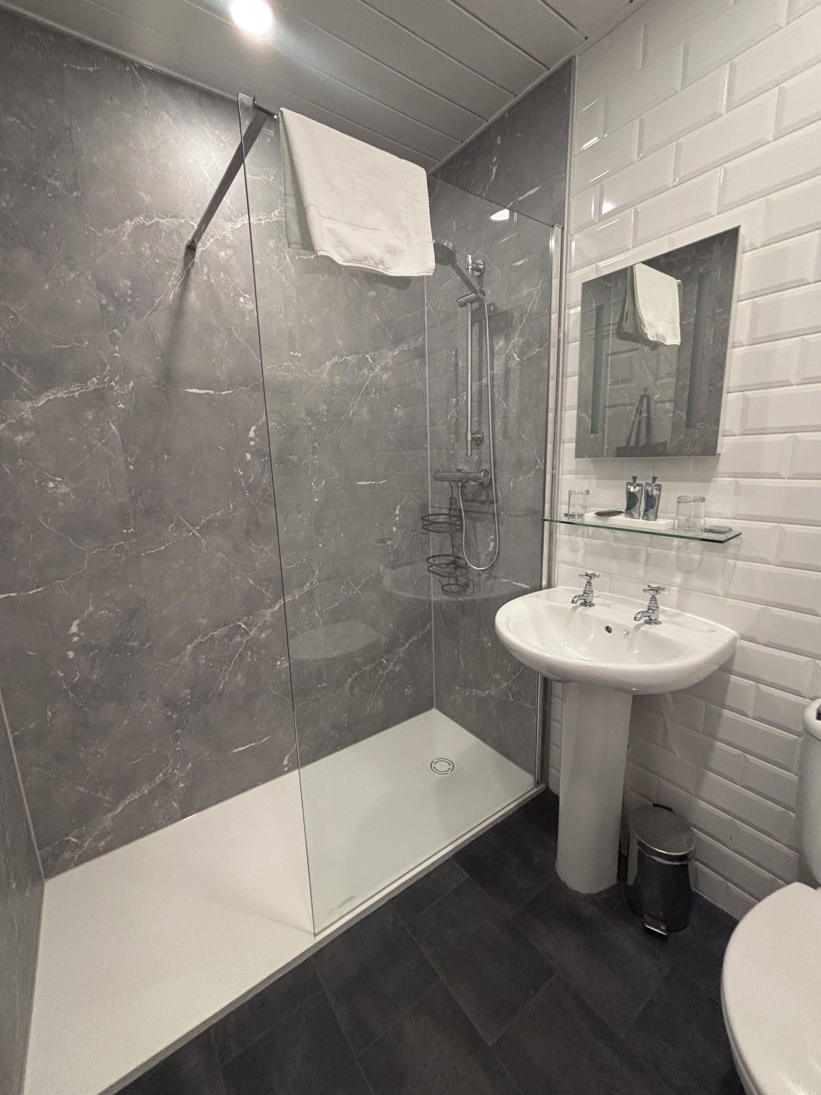 A modern bathroom with a glass-enclosed shower, a white pedestal sink, and a large mirror above the sink.