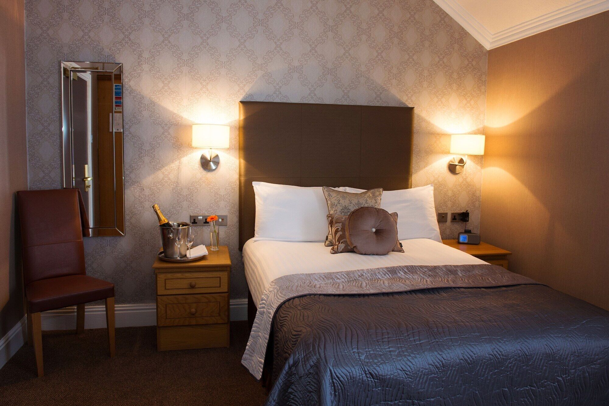 Ein Hotelzimmer mit Bett, Nachttischen, einem Sessel, einem Spiegel und einer Minibar.