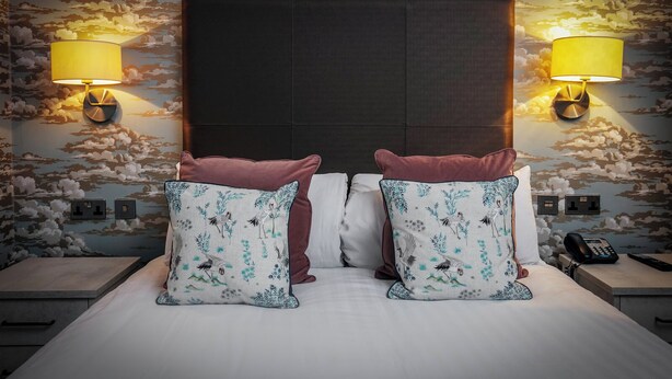 A hotel room with a bed, two nightstands, two lamps, and a wall with a cloud pattern.